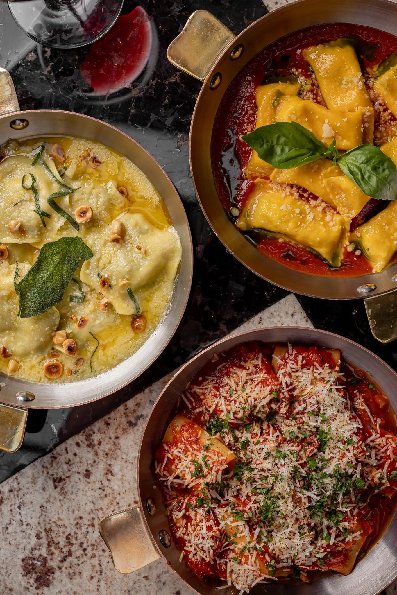 Three plates of Pasta on the counter with a glass of red wine